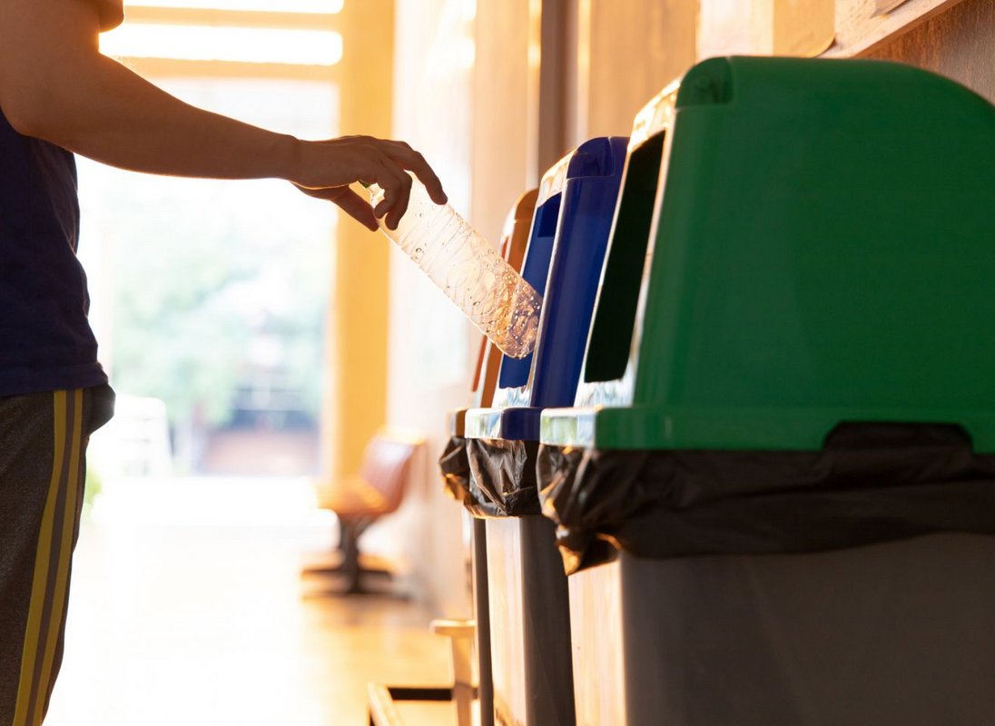 Poubelles de tri alignées, une main jette une bouteille en plastique